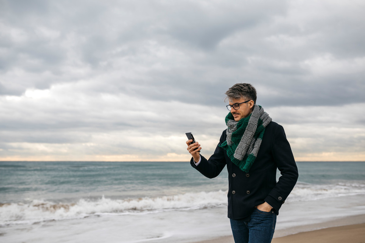 Man walking on beach looking at phone
