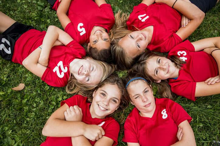 girls sport teammates laying in grass in a circle looking up